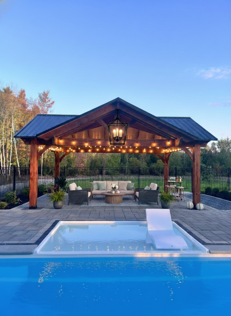 NORWEH TImber Frame High Top Pavilion with string lights and lounge seating beside a modern swimming pool at dusk